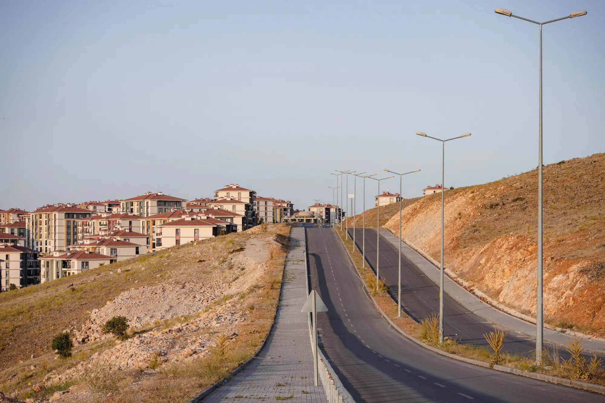 A new road climbing past freshly built apartment blocks on bare hillside at the edge of a city