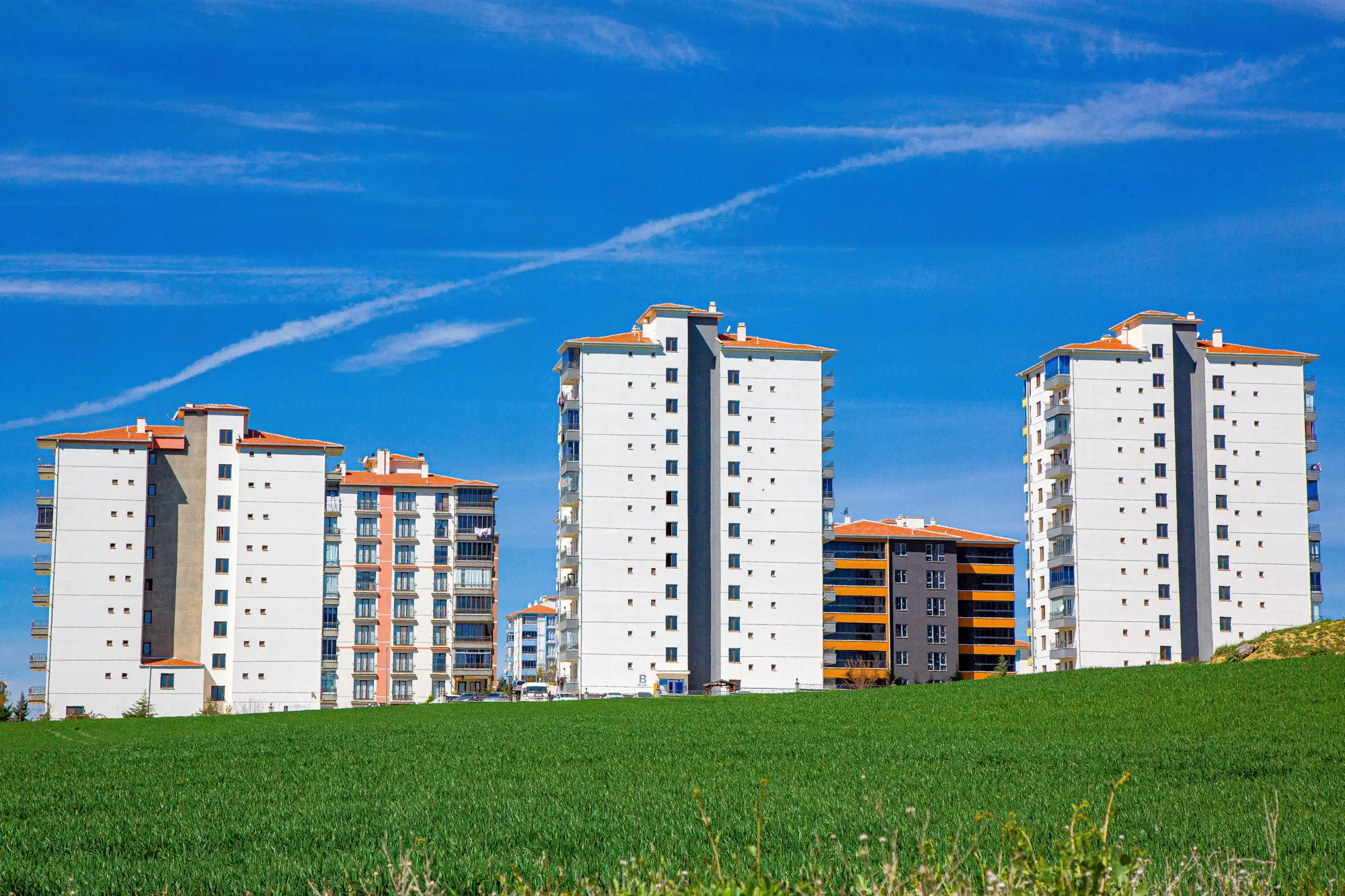New apartment towers standing at the edge of a green field under a blue sky